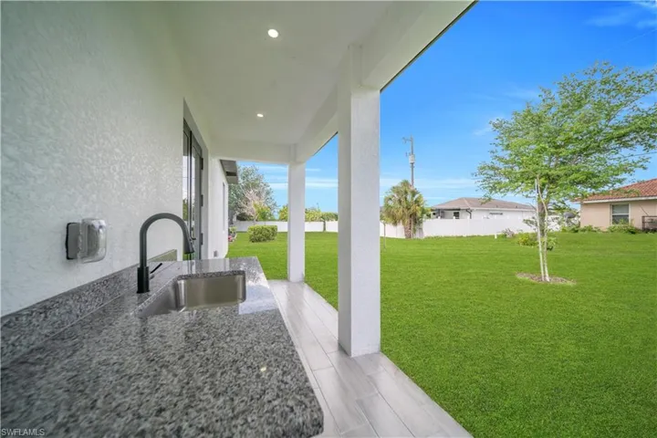 Covered patio with a built-in outdoor sink featuring a matte black faucet, granite-style countertop, and recessed lighting