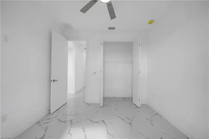 Light-filled interior featuring white walls, marble-look tile flooring, and a ceiling fan