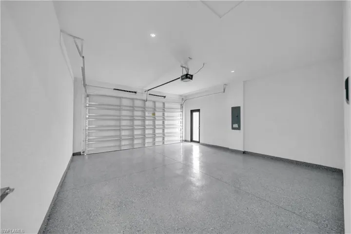 Spacious garage featuring a finished floor coating, painted walls, an overhead garage door, a side entry door, and recessed lighting