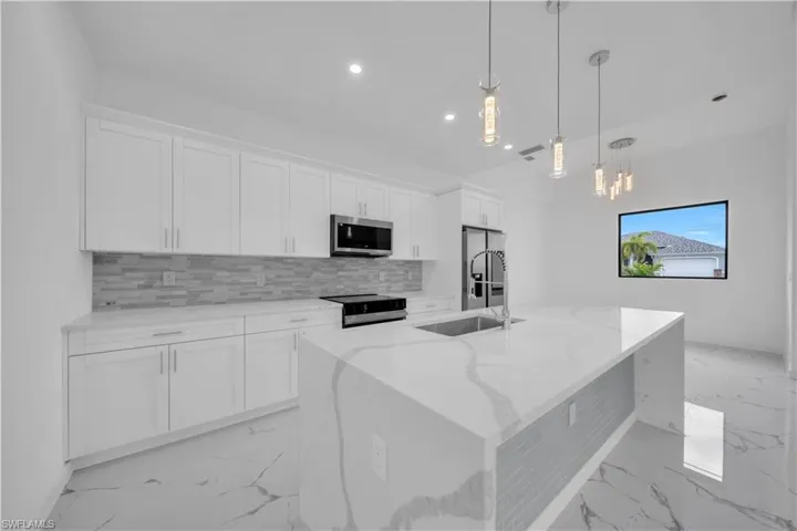 Modern kitchen featuring a waterfall island, stainless steel appliances, white shaker cabinetry, and pendant lighting