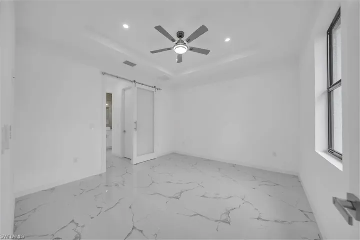 Spacious room featuring large format tile flooring, a tray ceiling with recessed lighting, and a contemporary ceiling fan