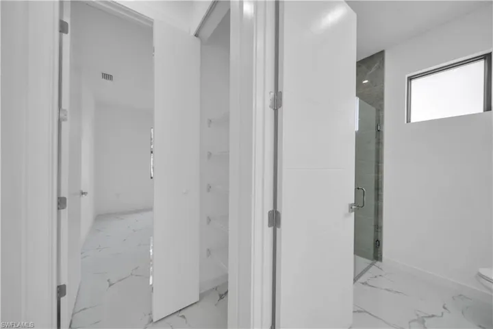 Bathroom featuring a glass-enclosed shower with tile surround, a built-in pantry with shelving, and white tile flooring