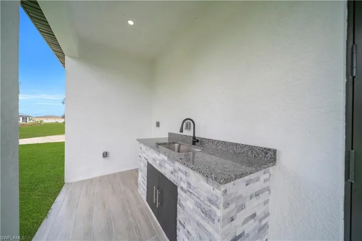 Outdoor kitchen featuring a stone-clad base, granite countertop, and integrated sink with a matte black faucet