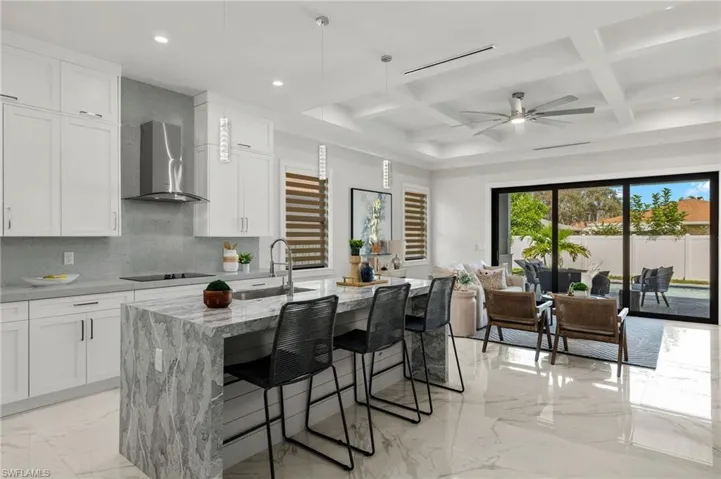 Kitchen with wall chimney range hood, a sink, marble finish floor, black electric stovetop, and light stone countertops