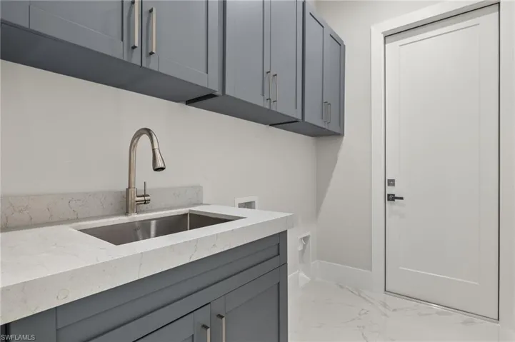 Laundry room with marble finish floor, a sink, hookup for a washing machine, baseboards, and cabinet space