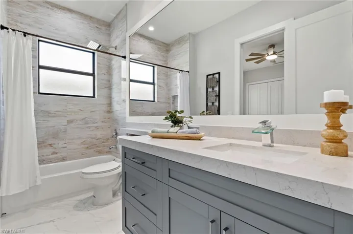 Full bath featuring marble finish floor, toilet, vanity, shower / bath combo with shower curtain, and ceiling fan