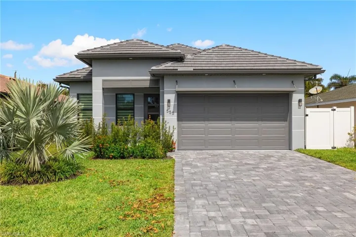 Prairie-style home featuring a tile roof, a front lawn, an attached garage, stucco siding, and decorative driveway