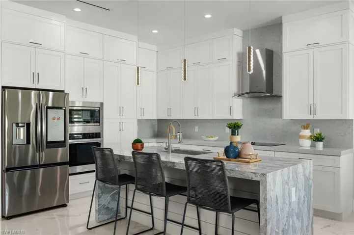 Kitchen with marble finish floor, stainless steel appliances, light stone countertops, wall chimney exhaust hood, and white cabinetry