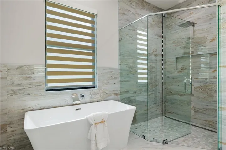 Bathroom with a shower stall, a wealth of natural light, a freestanding tub, and tile walls