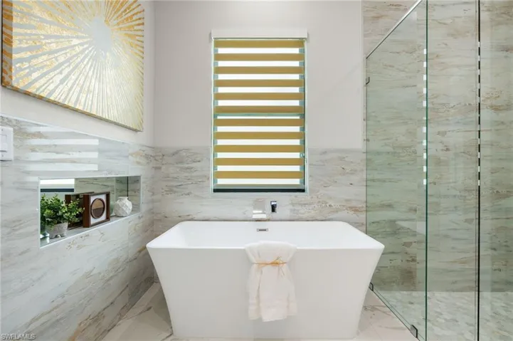 Full bath featuring marble finish floor, a healthy amount of sunlight, and tile walls