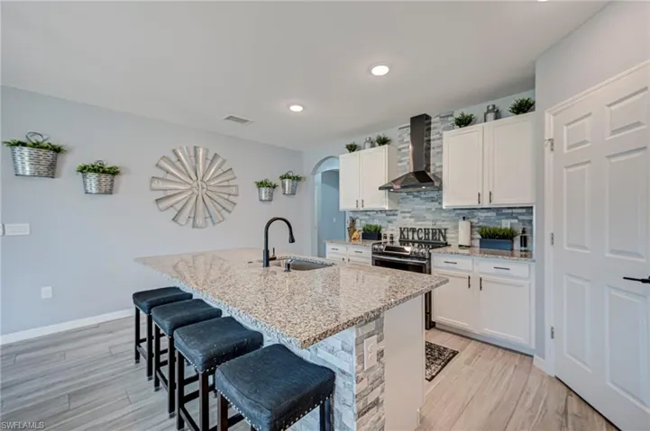 Kitchen with a breakfast bar area, white cabinetry, light stone counters, light wood-style floors, and a kitchen island with sink