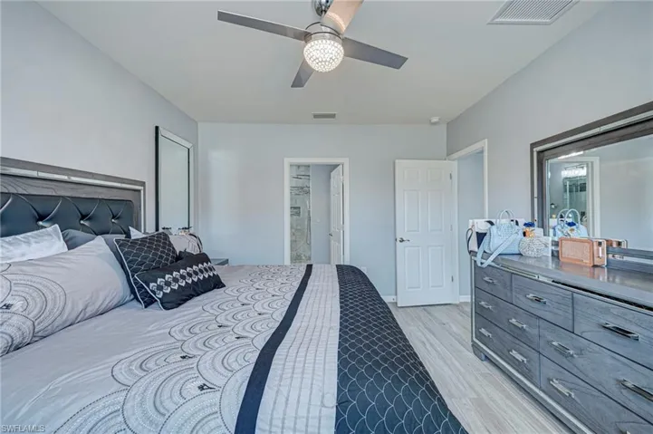 Bedroom with ensuite bathroom, ceiling fan, and light wood-style floors