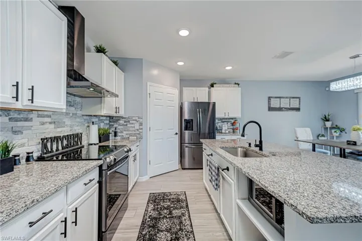 Kitchen featuring stainless steel appliances, light stone countertops, white cabinetry, a kitchen island with sink, and light wood-type flooring
