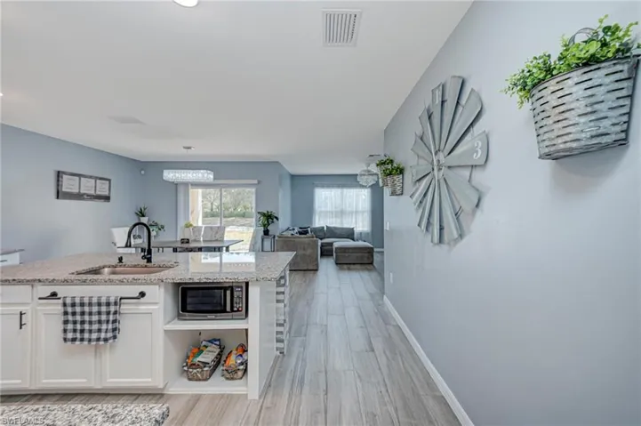Kitchen with open floor plan, white cabinets, light stone countertops, light wood-type flooring, and stainless steel microwave