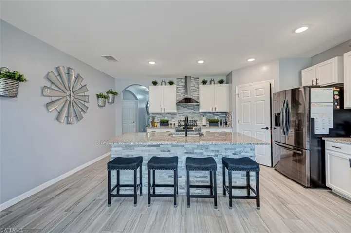 Kitchen featuring stainless steel appliances, arched walkways, white cabinetry, light stone countertops, and a breakfast bar area