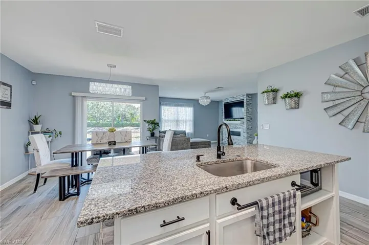 Kitchen featuring light wood-style floors, light stone countertops, white cabinetry, a center island with sink, and open floor plan
