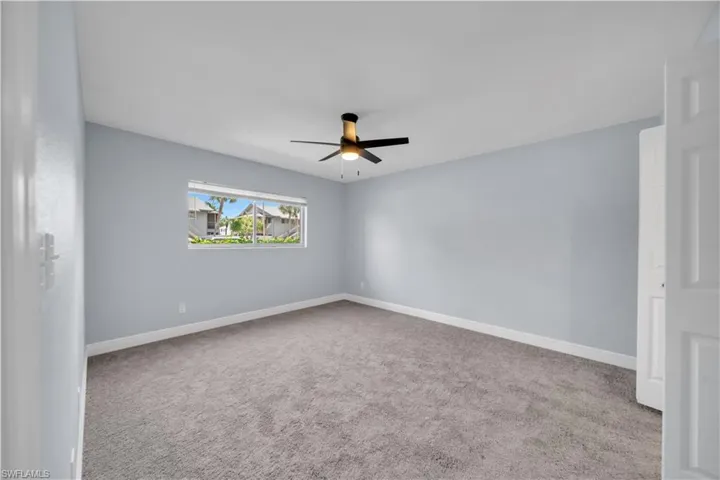 Spacious room featuring gray carpeting, a large window, a ceiling fan with light fixture, and a solid core door
