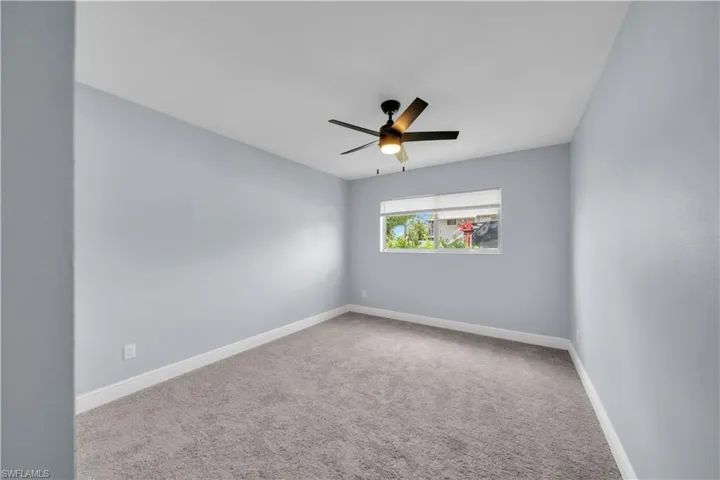 Spacious room featuring light gray walls, gray carpet, white baseboards, and a window with white blinds