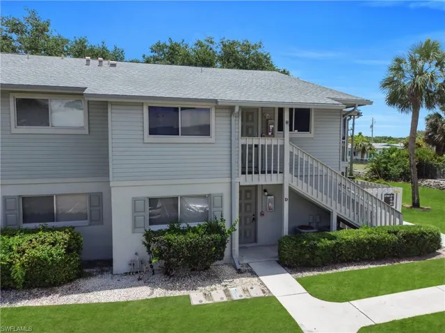 Two-story condominium building featuring horizontal siding, a light gray shingle roof, and a prominent exterior staircase