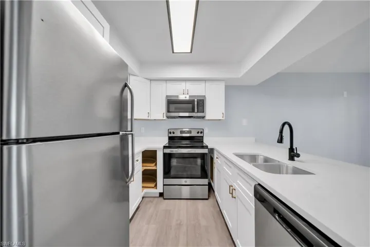 Modern kitchen featuring stainless steel appliances, white cabinetry, light countertops, a double basin sink, and wood-finish flooring