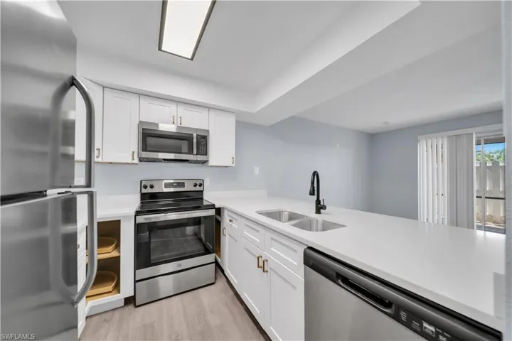 Modern kitchen featuring white cabinetry with gold-tone hardware, stainless steel appliances, and light-tone countertops