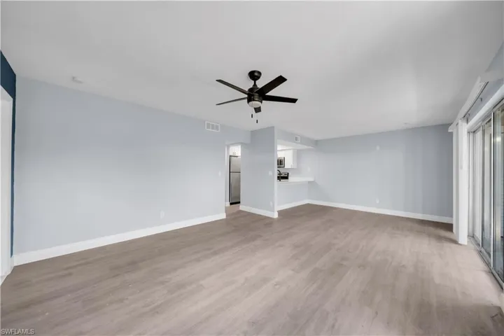 Open concept living area featuring wood-finish flooring, light blue wall paint, and a ceiling fan with dark blades