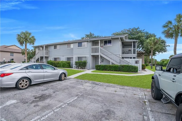 Two-story residential building featuring light grey siding, multiple exterior staircases, and a screened balcony