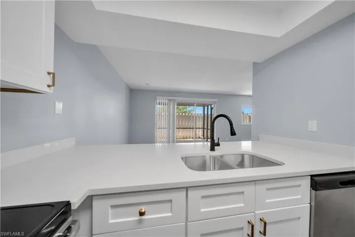 Kitchen featuring white shaker-style cabinetry with gold-tone hardware, white countertops, and a stainless steel double basin sink with a matte black faucet