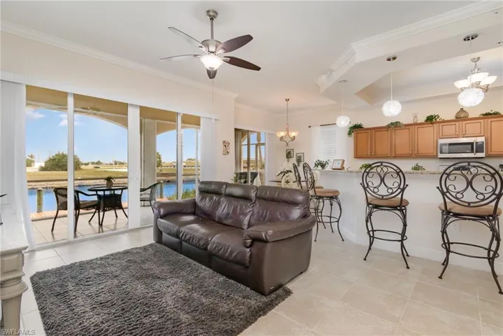 Living area with baseboards, crown molding, light tile patterned floors, and ceiling fan with notable chandelier