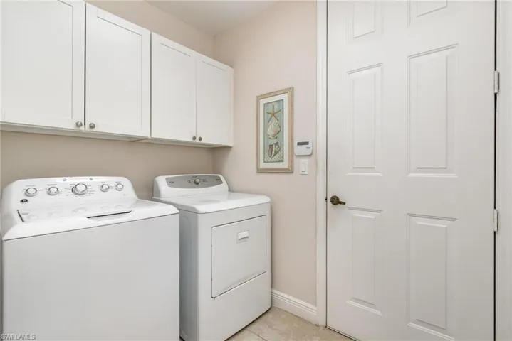 Clothes washing area with baseboards, independent washer and dryer, light tile patterned floors, and cabinet space