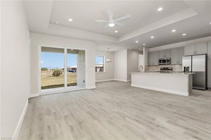 Unfurnished living room featuring light hardwood / wood-style floors, sink, ceiling fan, and a raised ceiling. Finishes may vary, pictures for illustration purposes only