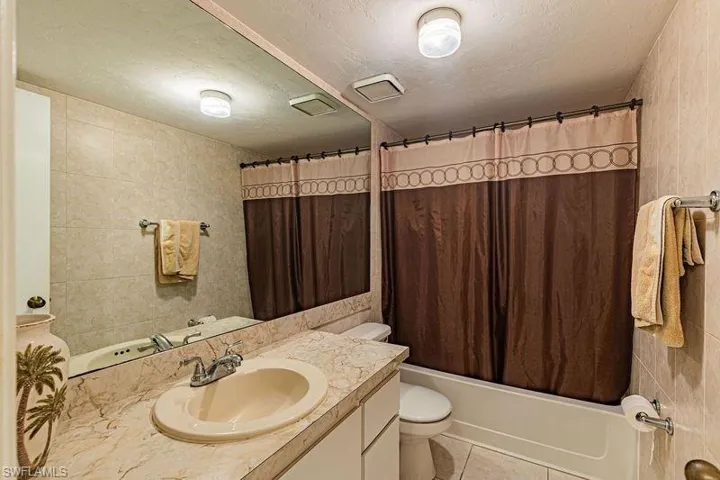 Full bath with a textured ceiling, vanity, shower / bath combo with shower curtain, light tile patterned floors, and tile walls