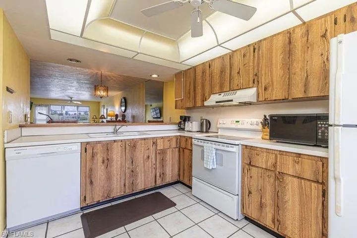 Kitchen featuring white appliances, ceiling fan, light countertops, and wood finish cabinets