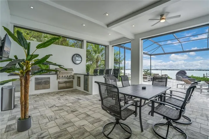 Sunroom / solarium featuring a water view, an outdoor kitchen, a patio, ceiling fan, and healthy amount of natural light