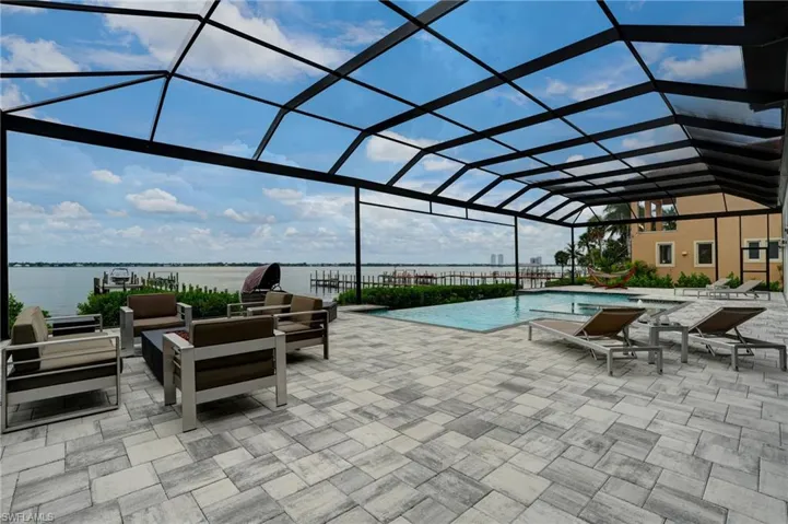 Outdoor pool with glass enclosure, a sunroom, a patio, and a water view