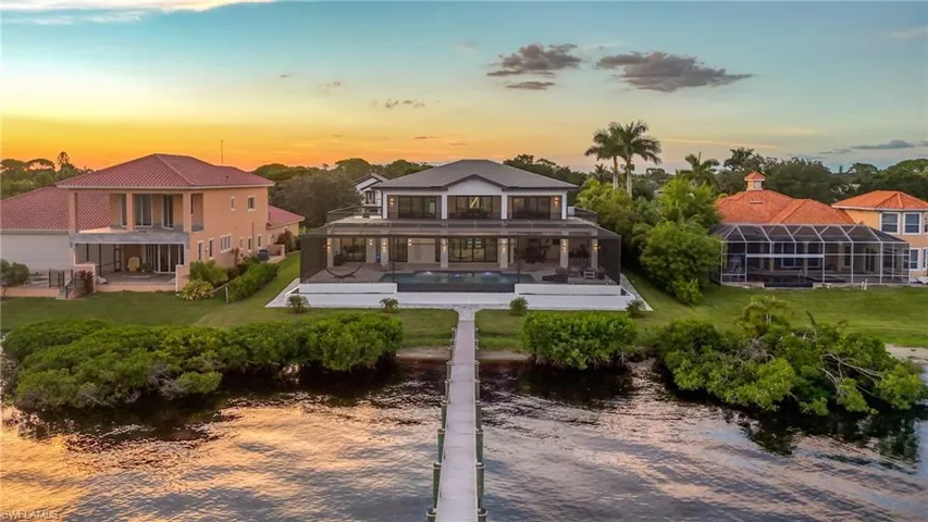 Back of property at dusk with a patio area, a yard, an outdoor pool, and a water view