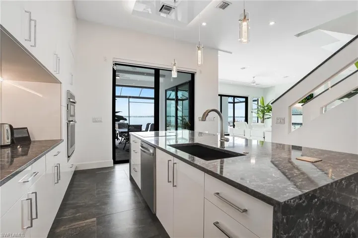 Kitchen featuring dark stone countertops, white cabinetry, a spacious island, hanging light fixtures, and stainless steel appliances