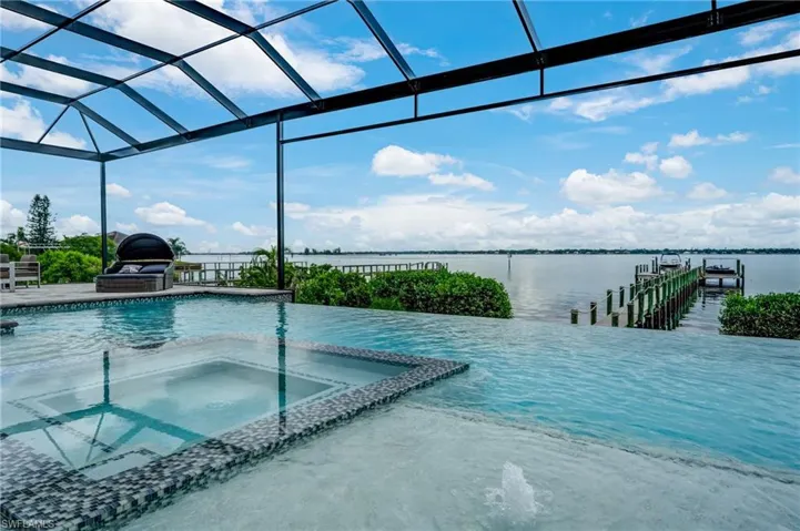 View of pool featuring a pool with connected hot tub, a boat dock, a lanai, a water view, and a sunroom