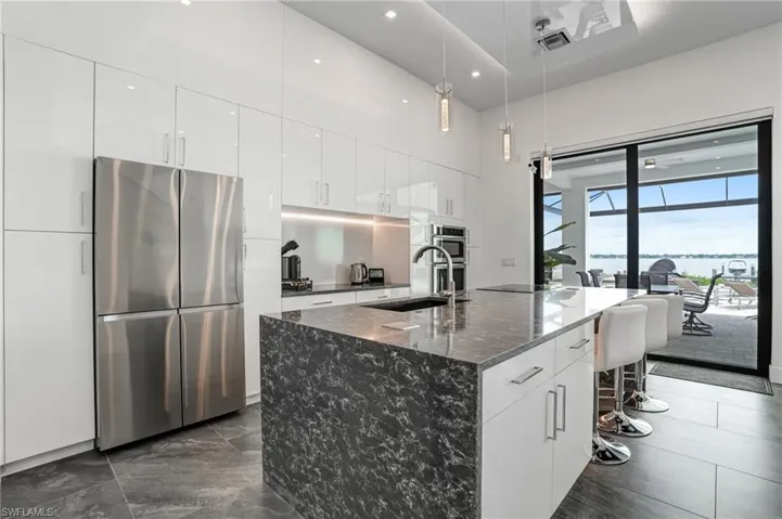 Kitchen featuring appliances with stainless steel finishes, a breakfast bar area, pendant lighting, dark stone counters, and an island with sink