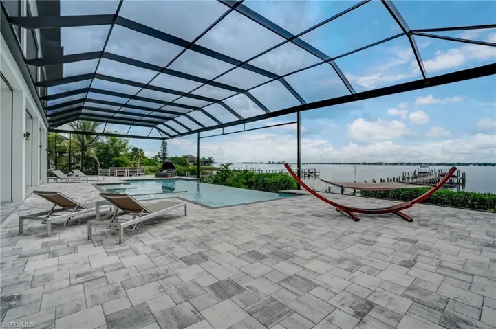 View of swimming pool featuring glass enclosure, a water view, a patio area, and an infinity pool