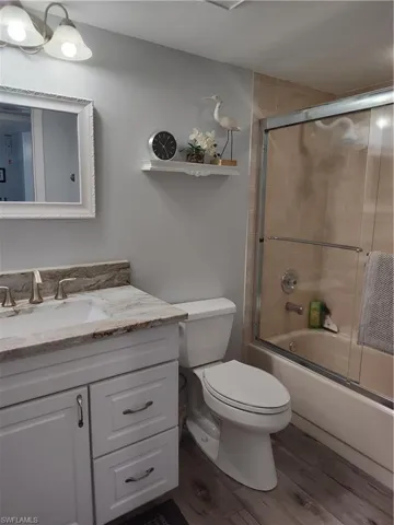 Full bathroom featuring hardwood / wood-style floors, toilet, enclosed tub / shower combo, and vanity