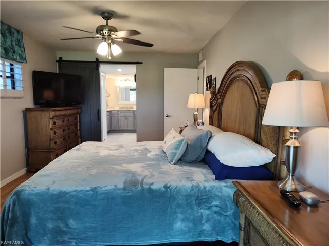 Bedroom with connected bathroom, multiple windows, a barn door, and ceiling fan
