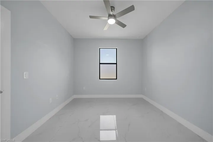 Neutral-toned room featuring a central window, ceiling fan with integrated lighting, light gray walls, and large format floor tiling