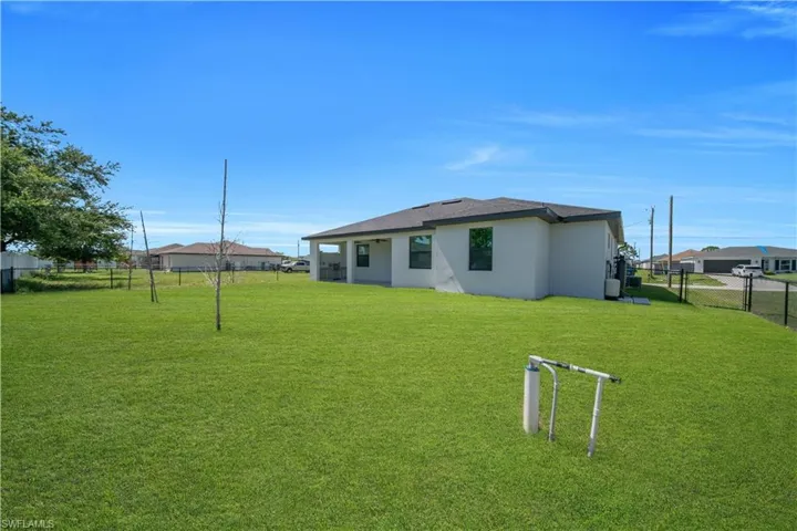 Expansive green lawn surrounds the property, featuring a covered patio area and partial fencing