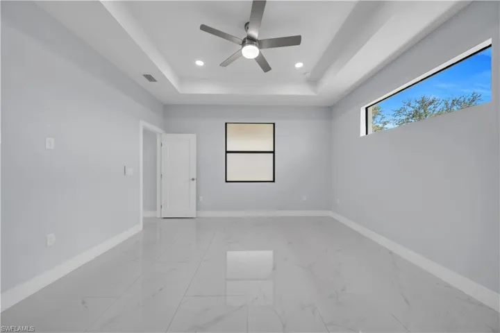 Spacious room featuring a tray ceiling with recessed lighting and a ceiling fan