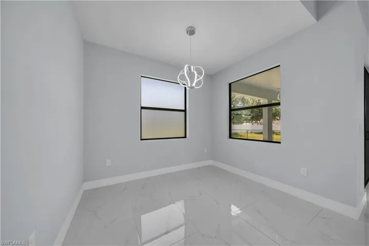 Bright interior room featuring a contemporary hanging light fixture, two windows with black frames, white baseboards, and large format light-toned tile flooring