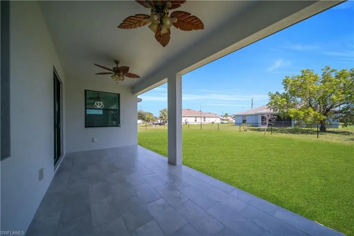 Expansive covered patio featuring large format tile flooring, twin ceiling fans, and a sliding glass door