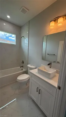 Bathroom featuring vanity, tub / shower combination, light marble finish flooring, and recessed lighting