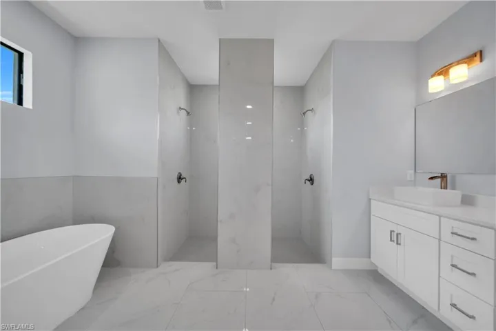 Spacious bathroom featuring twin walk-in showers with tiled walls, a freestanding soaking tub, single vanity with a vessel sink, and large format tile flooring