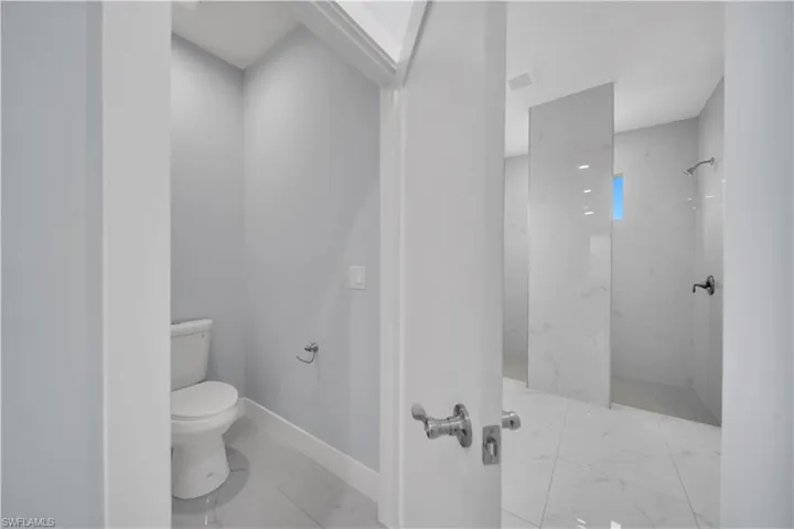 Bathroom featuring a toilet within a private alcove, white tile flooring, and a walk-in shower with a glass partition and wall-mounted shower head